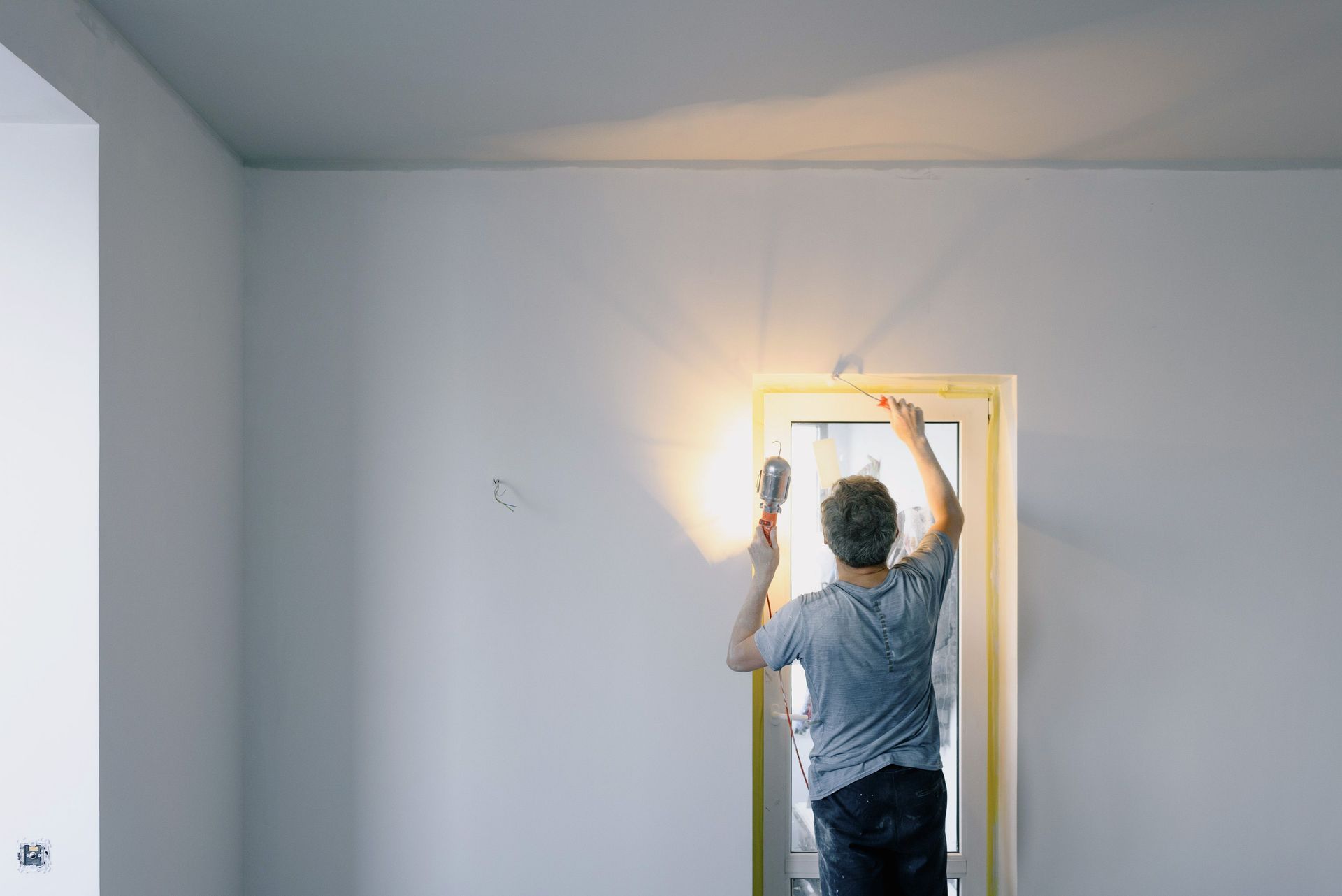 Back view of unrecognizable male in dirty clothes holding bright lamp while repairing door at home
